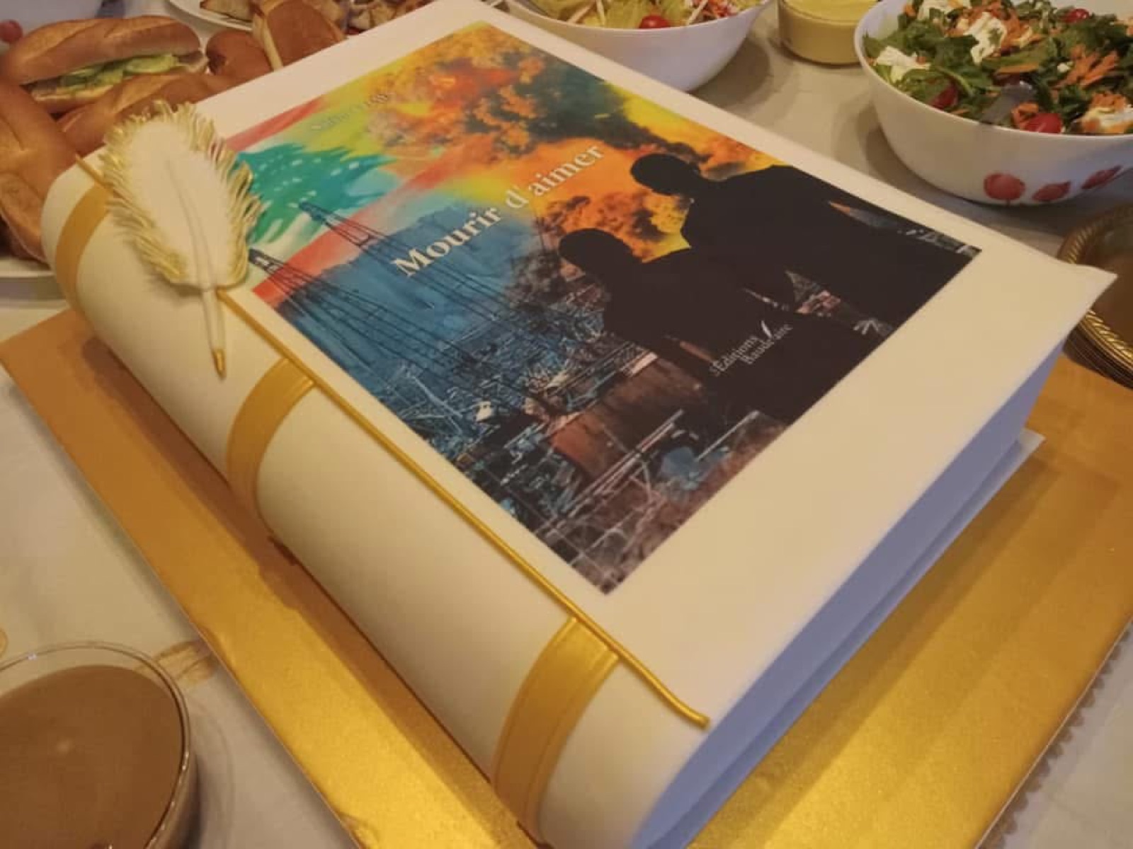 Gâteau en forme de livre à la couverture de Mourir d'aimer, plume dorée posée dessus