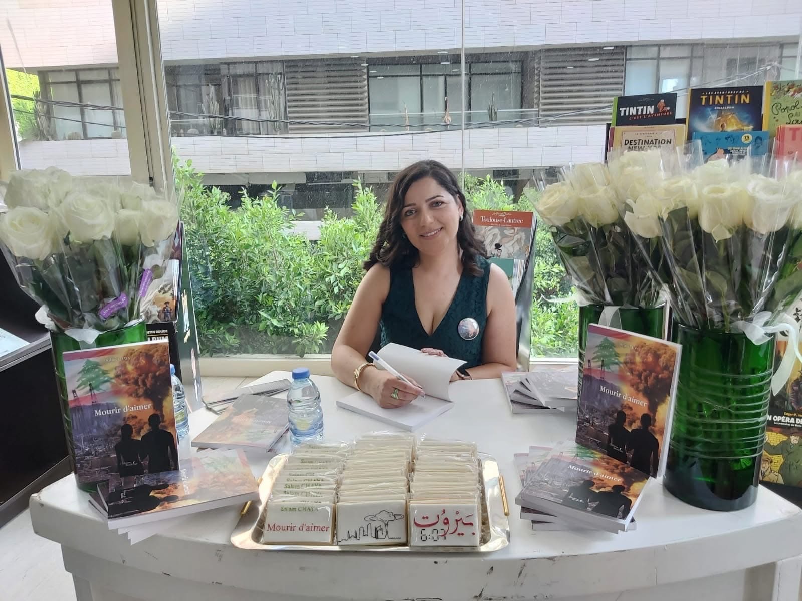 Salam Chaya à la table de dédicace, entourée de roses blanches, d'exemplaires de Mourir d'aimer et de biscuits « Beyrouth 6:07 »
