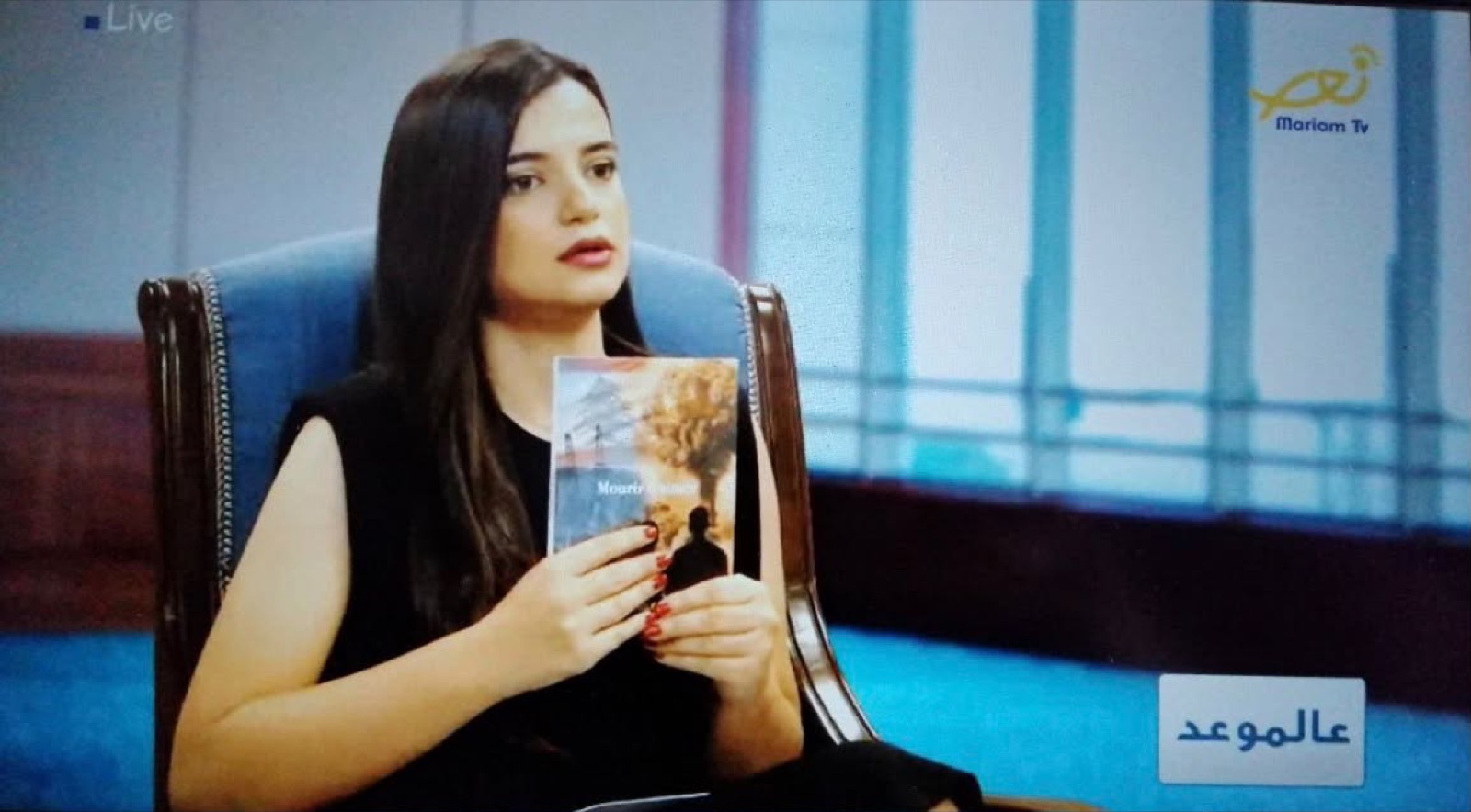 Plan de l'émission Mariam TV montrant Salam Chaya tenant son roman Mourir d'aimer face à la caméra