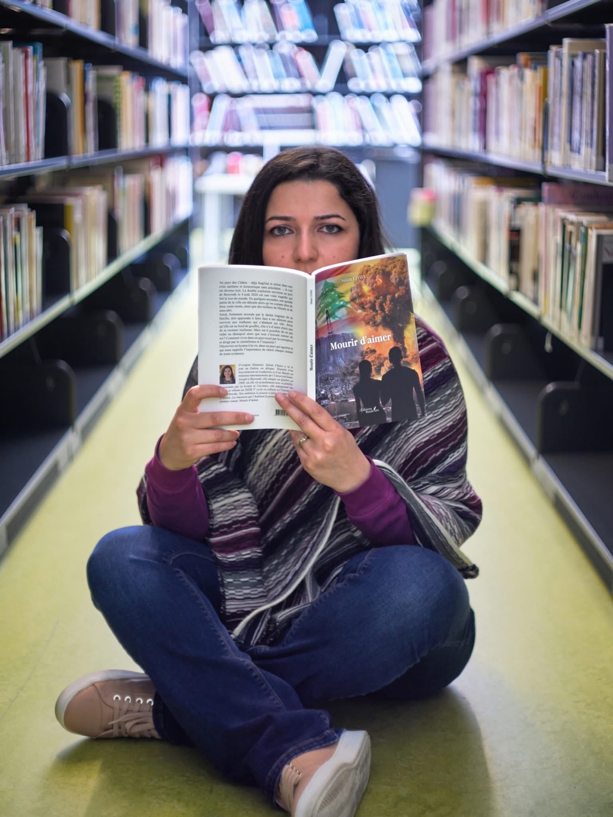 Salam Chaya assise au sol entre les rayonnages d'une bibliothèque, Mourir d'aimer ouvert devant son visage